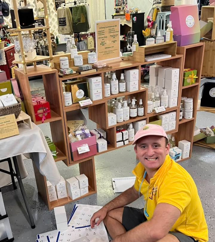 A Naturalistic Body Care team member beside shelves of body care products at a market display.